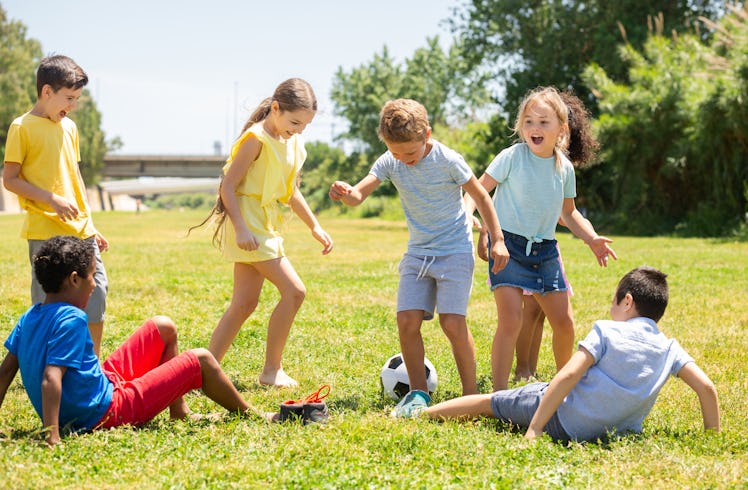 Group of happy schoolchildren playing football together in park