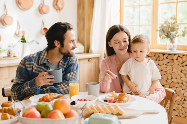 Morning breakfast at home. Young caucasian family of three, parents and infant toddler new born baby...