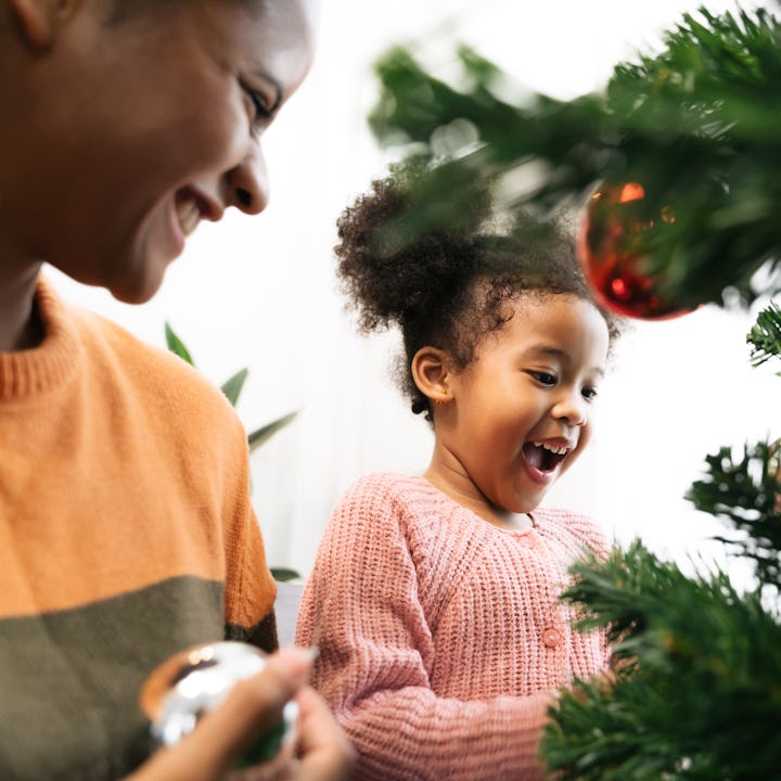 Mother and daughter african american girl decorating Christmas tree with ,arranging the christmas li...