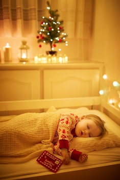 A little girl sleeps under the glow of a Christmas tree in her bedroom.