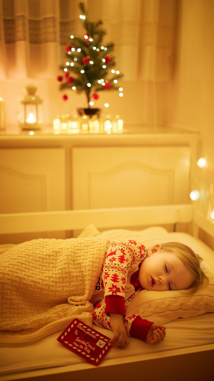 A little girl sleeps under the glow of a Christmas tree in her bedroom.