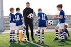 年轻教练在足球场上教孩子们。教练向男生解释训练规则。足球……