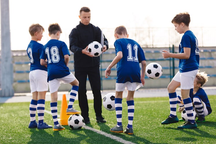 Young coach teaching kids on football field. Trainer explains to schoolboys training rules. Football...