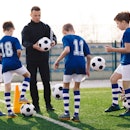 Young coach teaching kids on football field. Trainer explains to schoolboys training rules. Football...