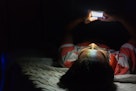 亚洲年轻男子在黑暗房间的床上使用手机。瘦家伙玩他的智能手机上…