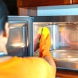 Close up housemaid cleaning microwave oven inside with sponge in the kitchen.