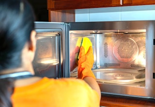 Close up housemaid cleaning microwave oven inside with sponge in the kitchen.