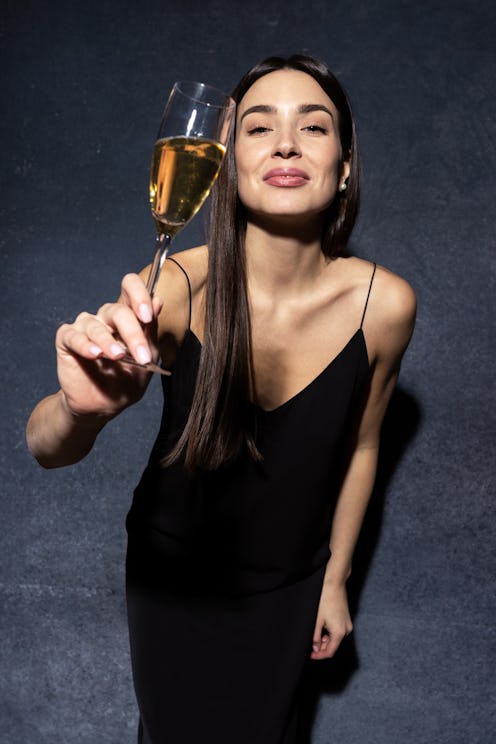 An attractive young woman in a black evening dress holds a glass of champagne. New Year's Eve Concep...