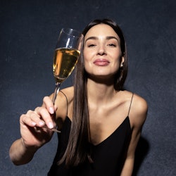 An attractive young woman in a black evening dress holds a glass of champagne. New Year's Eve Concep...