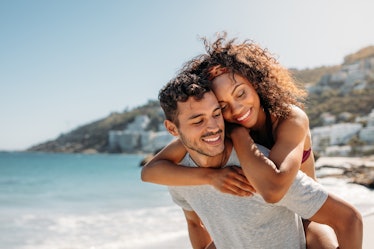 Happy man carrying a woman on his back walking on beach, thinking of their love horoscopes for 2023