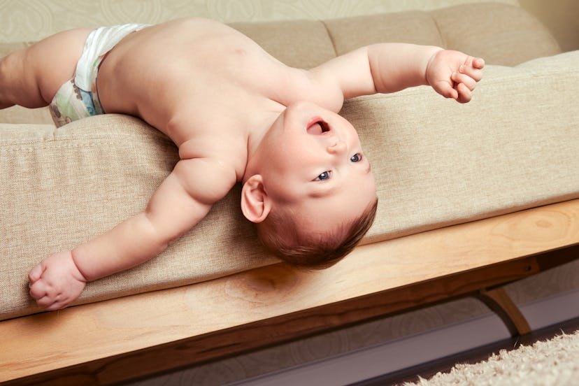 A baby boy lounges upside down on a couch. Boy names that mean love include Milos.