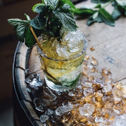 Mint Julep cocktail in glass on Bourbon whiskey barrel with crushed ice 