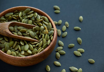 pumpkin seeds in a wooden bowl and vintage scoop. Close up on a black background. copy space for tex...