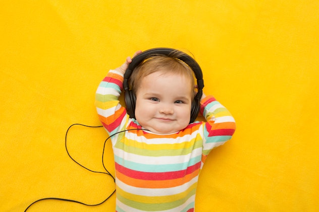 A baby with headphones on a yellow background; baby boy names that mean love include "Amadeus."