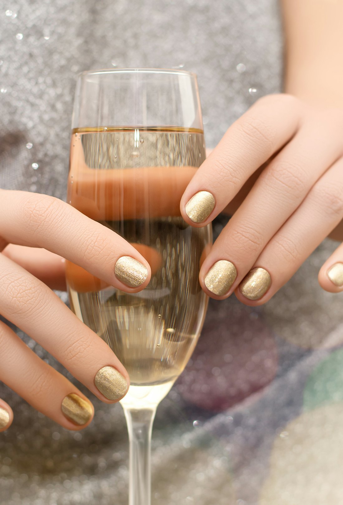 Hands holding a champagne glass with gold nail polish, an idea for NYE nails.