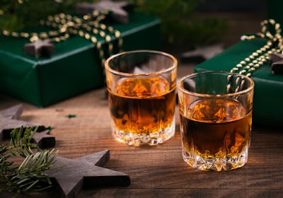 Two shot glasses of whiskey or bourbon with Holiday decoration on wooden background. New Year, Chris...