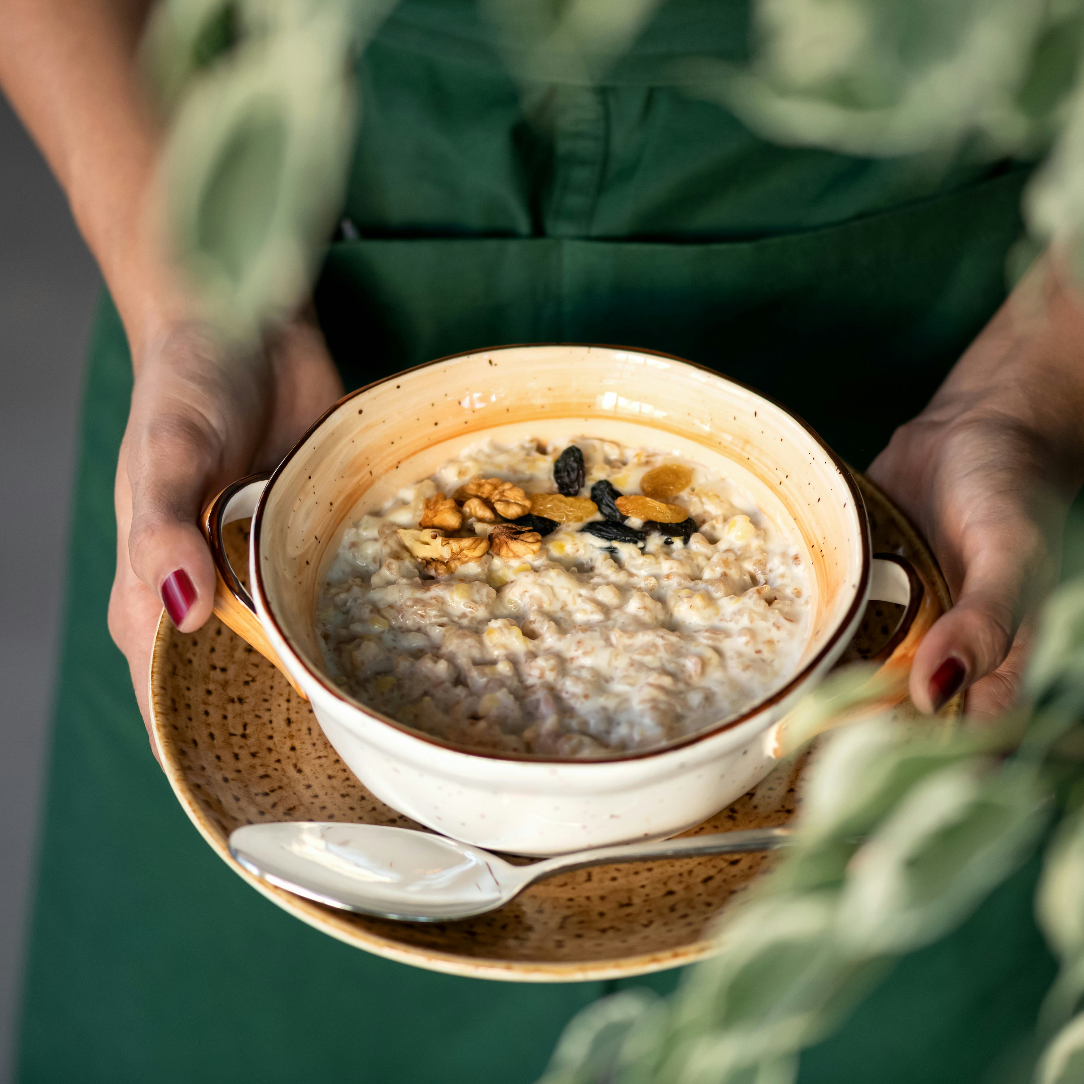 Traditional english breakfast. Woman holds bowl of cereal oatmeal or porridge with milk, raisins and...