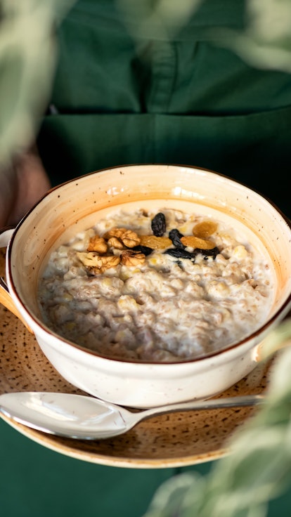 Traditional english breakfast. Woman holds bowl of cereal oatmeal or porridge with milk, raisins and...