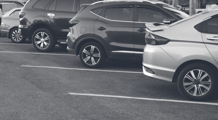 Closeup of rear, back side of blue car with  other cars parking in outdoor parking area in bright su...