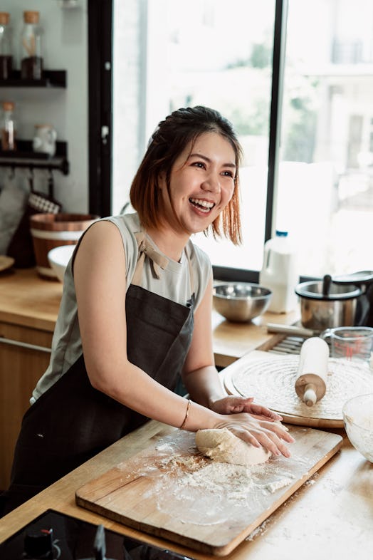 A cheerful woman kneads bread dough.