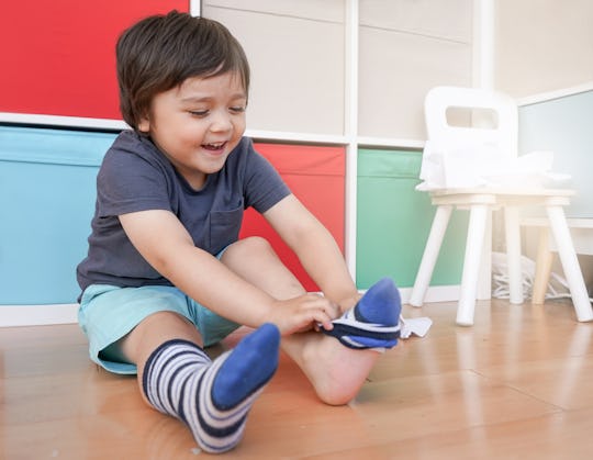 Cute little kid sitting next to tablet and learning how to put the socks on by him self, Happy Toddl...