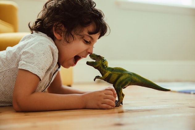 Adventurous young boy imitating a dinosaur toy while lying on the floor in his play area. Boy names ...