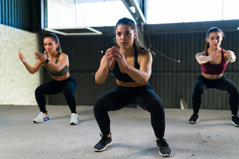 Beautiful women doing a cardio HIIT routine and squatting. Three fit women in sportswear working out...