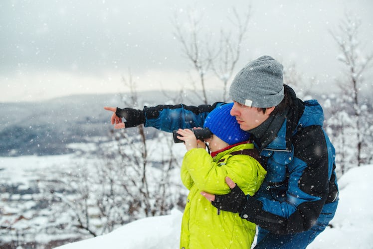 Dad and son outside in snowy weather, as the son using binoculars to gaze into the distance. at wint...
