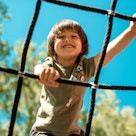 A child climbs up an alpine grid in a park on a playground on a hot summer day. children's playgroun...