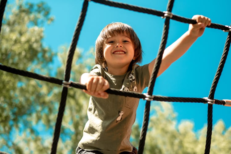 A child climbs up an alpine grid in a park on a playground on a hot summer day. children's playgroun...