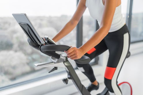 Exercise at home on spin bicycle fitness workout with screen. Woman training on stationary bike watc...