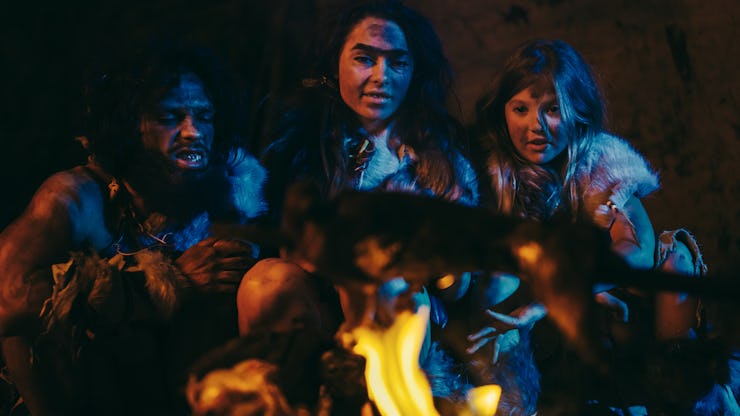 Neanderthal or Homo Sapiens Family Cooking Animal Meat over Bonfire and then Eating it. Tribe of Pre...