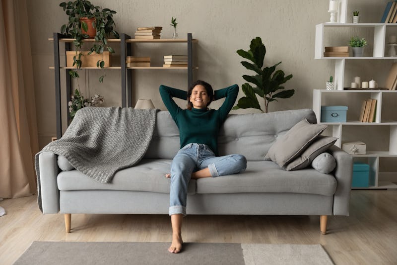 Sweet idleness. Lazy young hispanic lady sit in relaxed pose on big comfy sofa at living room interi...