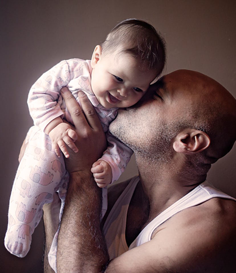 Lebanese American father playfully holds his baby daughter above his shoulders and kisses her left c...