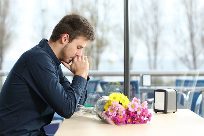 Sad man with bunch of flowers stood up in a date by his girlfriend in a coffee shop