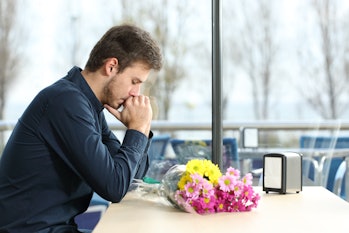 Sad man with bunch of flowers stood up in a date by his girlfriend in a coffee shop