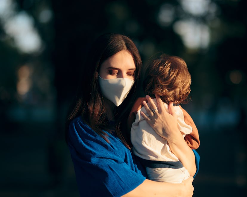 Worried Mother Wearing Face Mask Holding her Child. Mom feeling anxious for the future during pandem...