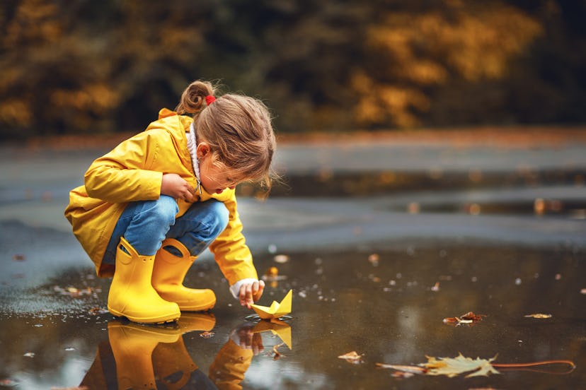 happy child girl with umbrella and paper boat in a puddle in   autumn on nature