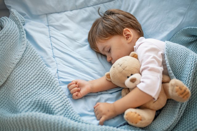 Healthy child, sweetest blonde toddler boy sleeping in bed holding her teddy bear. Adorable toddler ...