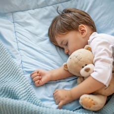 Healthy child, sweetest blonde toddler boy sleeping in bed holding her teddy bear. Adorable toddler ...