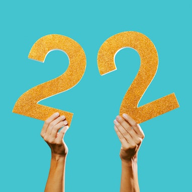 closeup of a man showing two golden three-dimensional numbers forming the number 22 on a blue backgr...