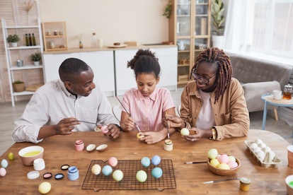 Portrait of modern African-American family painting Easter eggs together while sitting at wooden tab...