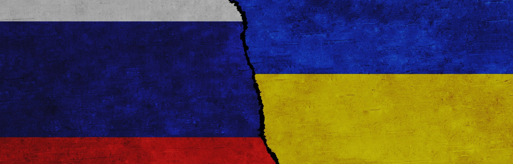Russia and Ukraine painted flags on a wall with a crack. Russia and Ukraine relations. Ukraine and R...