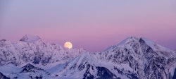 A full moon in the sky behind snow-covered hills. The spiritual meaning of February's full Snow Moon...
