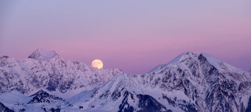 A full moon in the sky behind snow-covered hills. The spiritual meaning of February's full Snow Moon...