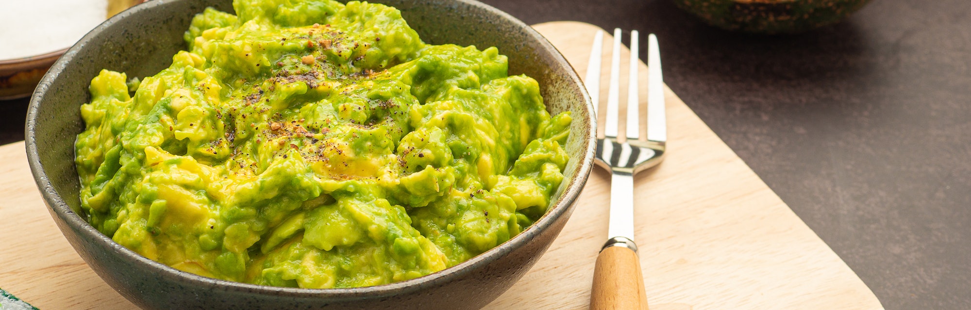Fresh guacamole on a dish placed on a cutting wooden board with ingredients for homemade guacamole: ...