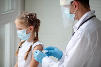 A doctor in a protective suit makes the child  in a medical mask a shoulder shot . Coronavirus vacci...