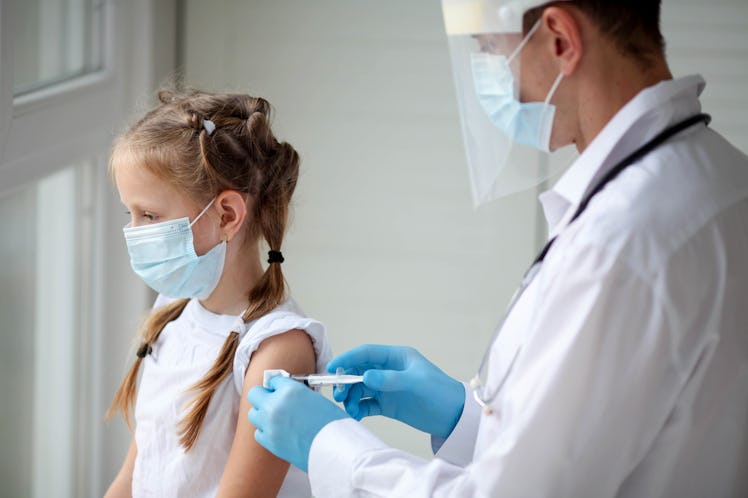 A doctor in a protective suit makes the child  in a medical mask a shoulder shot . Coronavirus vacci...