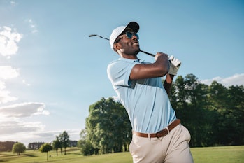 Smiling african american man in cap and sunglasses playing golf   