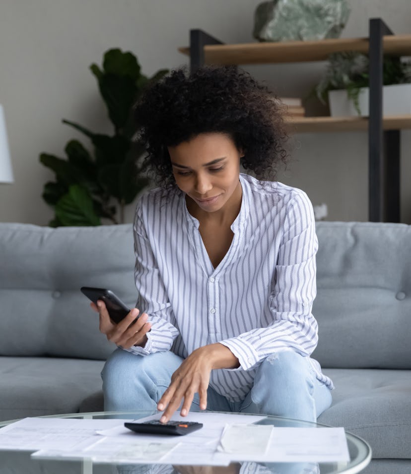 Accounting. Focused young black female sit on sofa pay domestic bills fees online using phone count ...